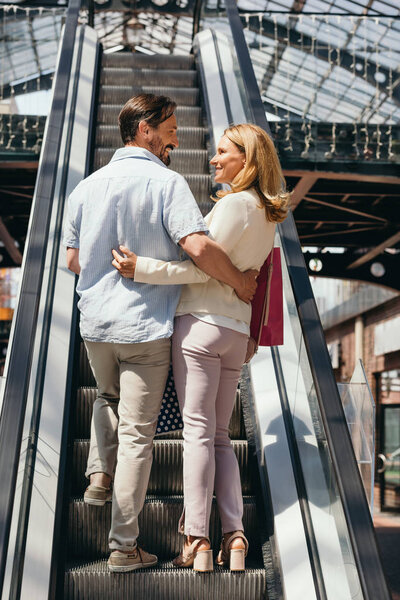back view of couple hugging on escalator in shopping mall