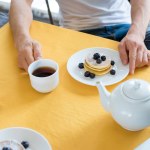 Vista parcial do homem sentado à mesa com café da manhã em casa