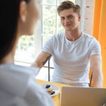 Selective focus of smiling man looking at girlfriend at table with breakfast and laptop at home