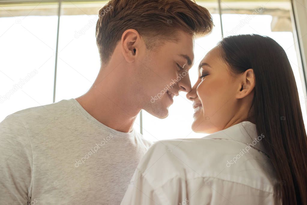 side view of smiling multicultural couple looking at each other at home
