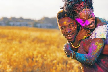 Afrika kökenli Amerikalı çift holi Festivali buğday alanında piggybacking gülüyor