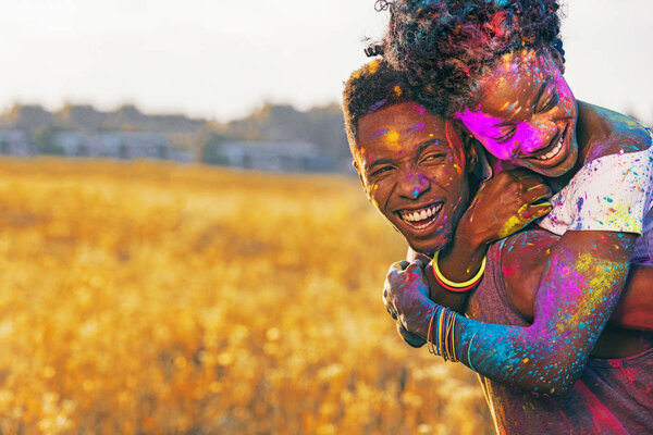 laughing african american couple piggybacking at holi festival in wheat field