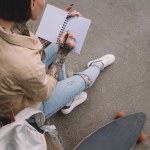 High angle view of tattooed woman with skateboard writing in empty textbook