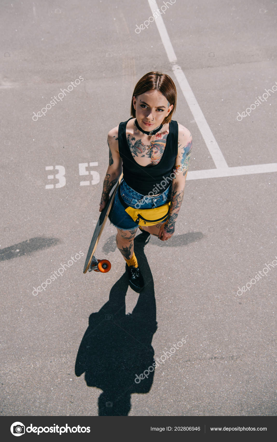 高角度的时尚纹身女孩持有滑板和看在停车场的相机——图库图片© IgorVetushko #202806946, image size:1068x1700