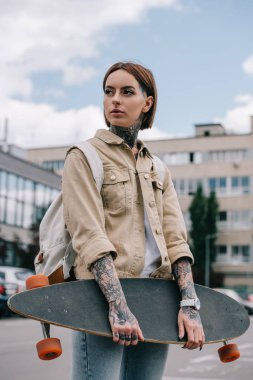 uzağa bakarak ve longboard Sokağı'nda tutan şık dövmeli kadın