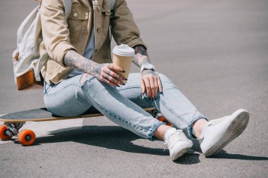 Kağıt bardak kahve ile kaykay üzerinde oturan dövmeli kadın resim kırpılmış 