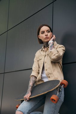 kaykay siyah duvara tutan çekici dövmeli kadın düşük açılı görünümü 