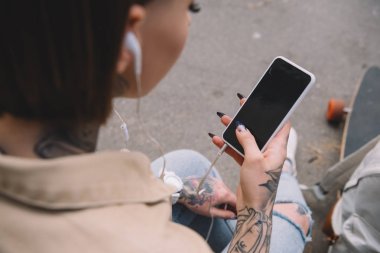 seçici odak içinde müzik dinlemek ve smartphone boş ekran ile tutarak kulaklık dövmeli kadın