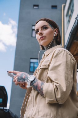 kulaklık smartphone ile müzik dinlemek içinde dövmeli kadın düşük açılı görünüş 