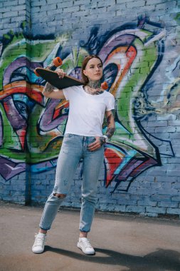 dövmeli yakınındaki duvara graffiti ile omuz üzerinde kaykay tutan çekici kız