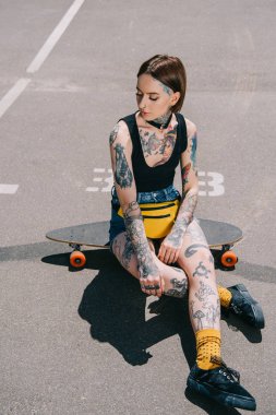Otopark kaykay üzerinde oturan dövmeler ile şık genç kadın 