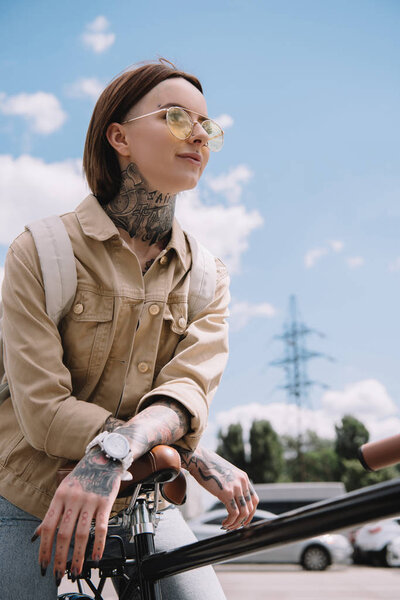 low angle view of stylish tattooed woman standing with bicycle at street 