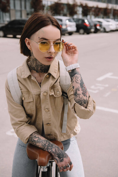 attractive stylish tattooed woman standing with bicycle at street 