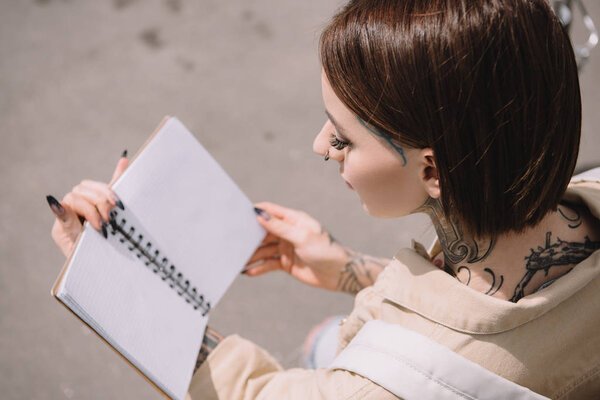 high angle view of stylish tattooed woman holding blank notebook 
