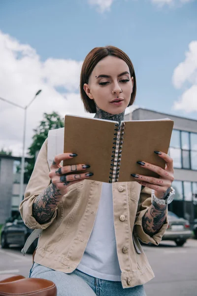 时尚纹身女性在街头阅读教科书的低角度观 — 免费的图库照片