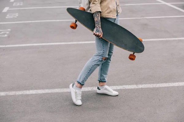 Περικομμένη Εικόνα Κομψή Τατουάζ Γυναίκα Κρατώντας Longboard Στο Πάρκινγκ — Δωρεάν Φωτογραφία