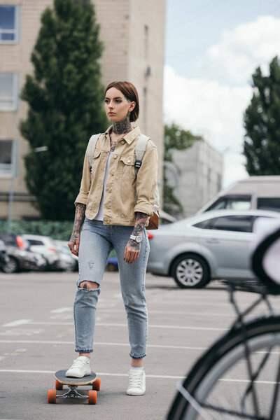 selective focus of stylish tattooed woman skateboarding at parking lot 