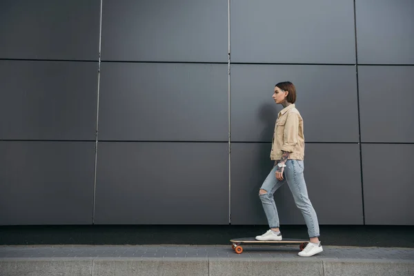Zijaanzicht Van Getatoeëerde Vrouw Stond Met Skateboard Tegen Zwarte Muur — Gratis stockfoto
