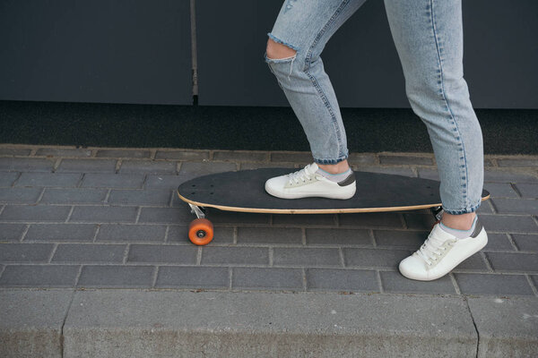 partial view of stylish woman skateboarding at street 