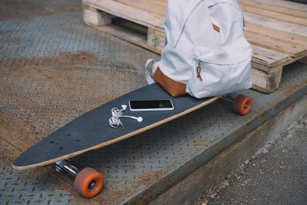 Nahaufnahme Von Kopfhörern Mit Smartphone Und Rucksack Auf Dem Skateboard — kostenloses Stockfoto