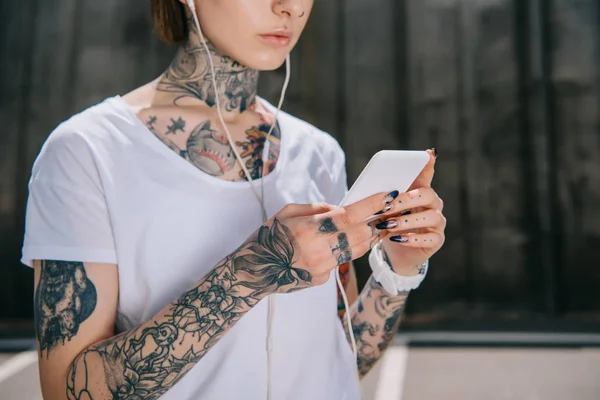 用智能手机播放耳机中纹身女性的裁剪图像 — 图库照片