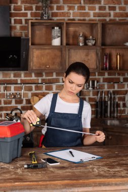 serious young repairwoman with measuring tape and clipboard at kitchen clipart