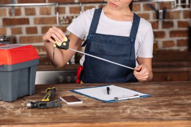cropped shot of young repairwoman with measuring tape and clipboard at kitchen clipart
