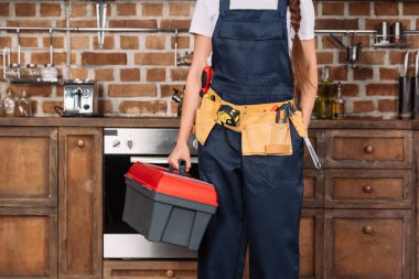 cropped shot of repairwoman with toolbox and toolbelt standing at kitchen  clipart