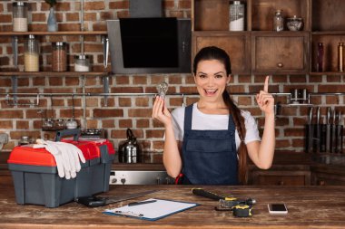 happy young repairwoman with light bulb pointing up and looking at camera clipart