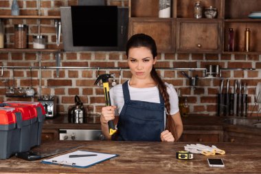 Mutfak ayakta ve kameraya bakarak çekiç ile ciddi genç repairwoman