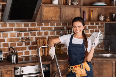 Genç repairwoman bir merdiven ve anahtarı ayakta mutfak at ile gülümseyen