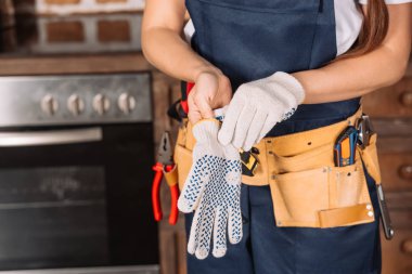 cropped shot of repairwoman putting on work gloves at kitchen clipart