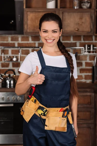 微笑年轻的 Repairwoman 站在厨房和显示拇指 — 图库照片