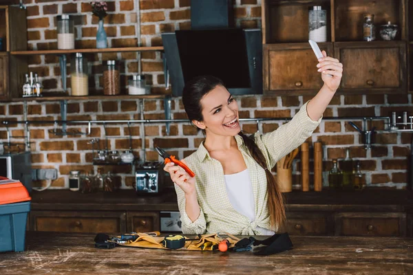 happy young woman taking selfie with pliers at kitchen