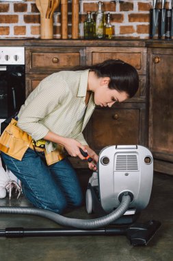çekici genç repairwoman tornavida ile elektrikli süpürge sabitleme
