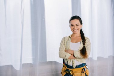 beautiful young repairwoman with toolbelt and crossed arms looking at camera clipart