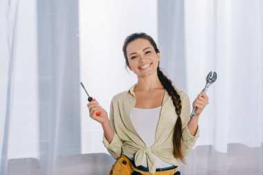 İngiliz anahtarı ve kameraya bakarak tornavida ile mutlu genç repairwoman