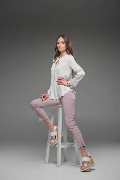 Modelo Femenino Elegante Sentado Silla Mirando Cámara Sobre Fondo Gris —  Fotos de Stock