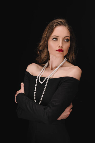 elegant woman in black dress posing and looking away isolated on black background 