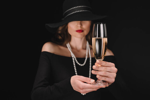 selective focus of champagne glass in hands of elegant woman with covered eyes by straw isolated on black background 