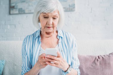 evde kanepede istirahat ederken smartphone kullanarak kadın kıdemli portresi