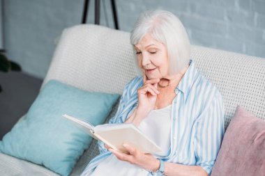 üst düzey kadın evde koltukta istirahat ederken kitap okuma