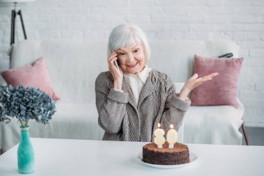 Evde Doğum günü pastası ile masada otururken smartphone üzerinde konuşmak mutlu kadın kıdemli portresi