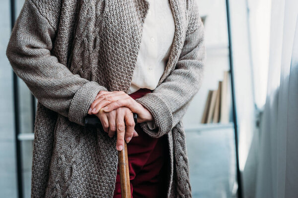 cropped shot of senior lady with wooden walking stick standing at home