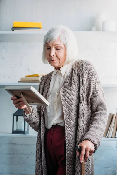 fotoğraf çerçevesi elinde evde bakarak baston ile örme ceket düşünceli üst düzey Bayan portresi