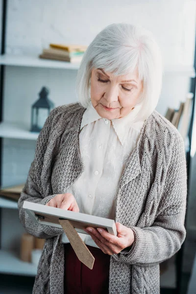 Örme ceket fotoğraf çerçevesi elinde evde bakarak düşünceli üst düzey Bayan portresi
