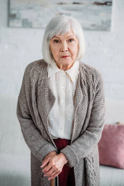 portrait of grey hair lady with wooden walking stick looking at camera at home