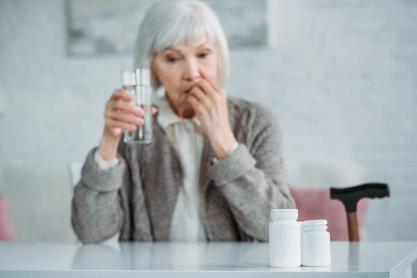 selective focus of grey hair woman with glass of water taking medicine at home