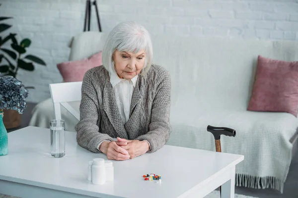 Retrato Mulher Idosa Pensativa Sentada Mesa Com Medicamentos Copo Água — Fotografia de Stock