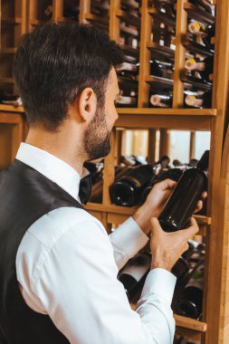 yakışıklı genç sommelier alarak şişe şarap mağazasında raf